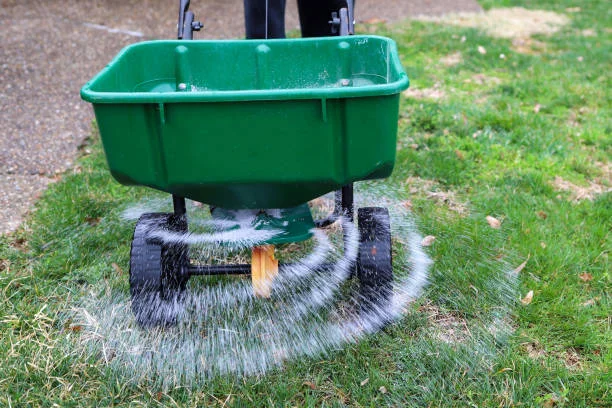 spreader applying fertilizer on a green lawn